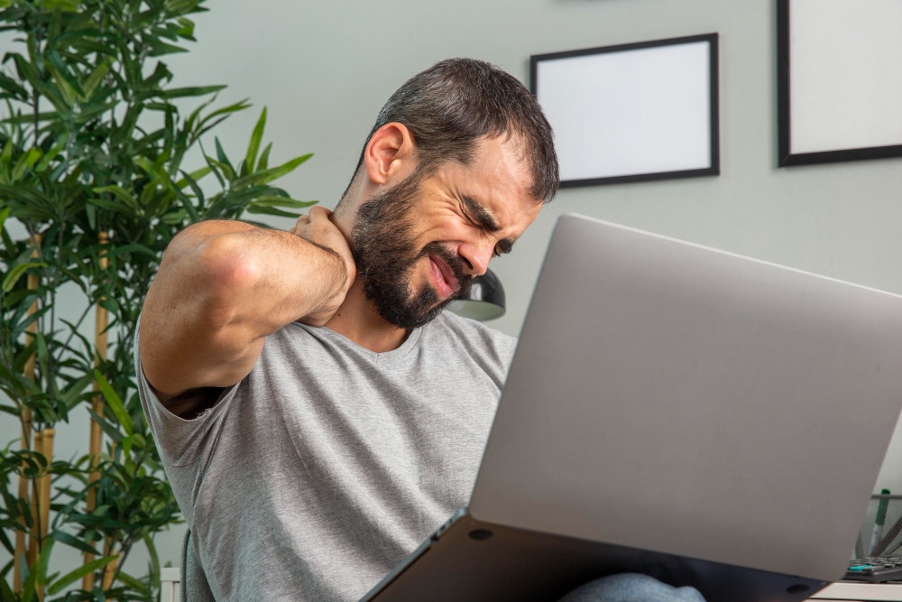 man experiencing neck pain while working from home laptop
