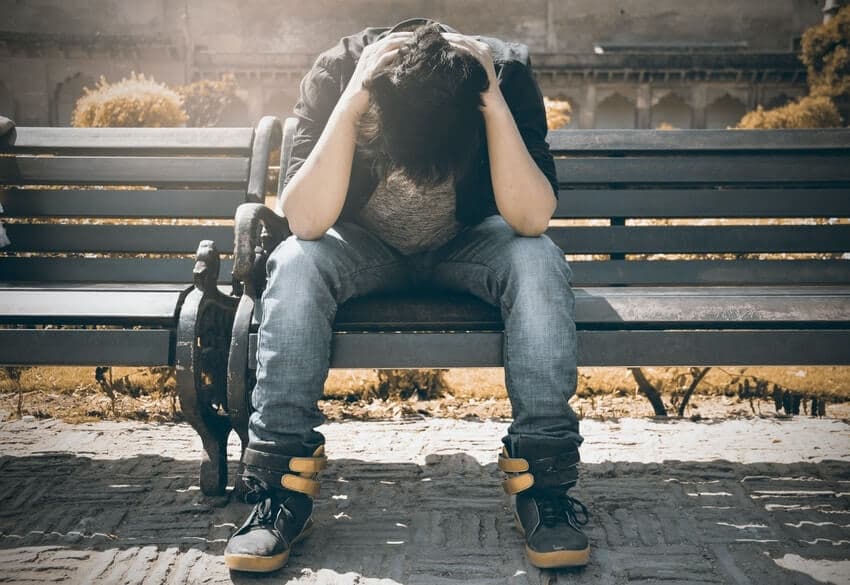 man holding his head down from anxiety on a bench