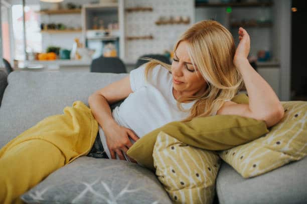 blonde woman in the sofa holding her stomach due to Crohn's disease