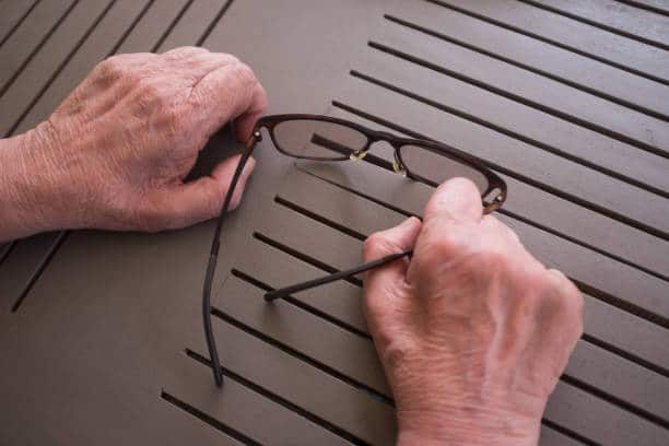 Elderly man's hands holding eyeglasses suffering Peripheral Neuropathy Pain.