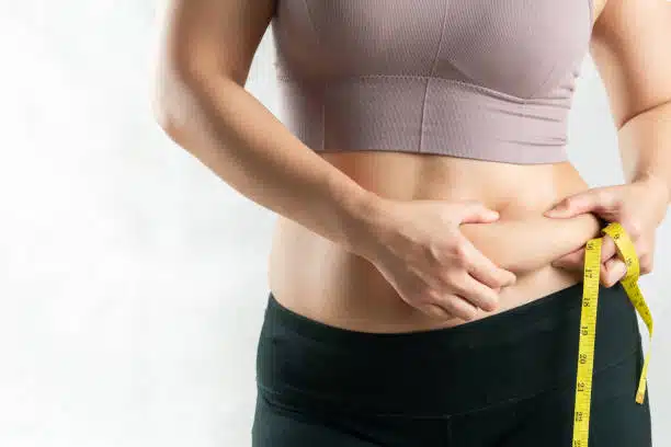 woman holding excessive belly fat with tape measure before taking an IV therapy for weight loss