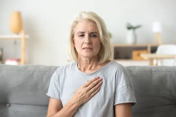 Senior woman having a heart condition problem sitting on the couch while catching her breathe caused of heart ache.