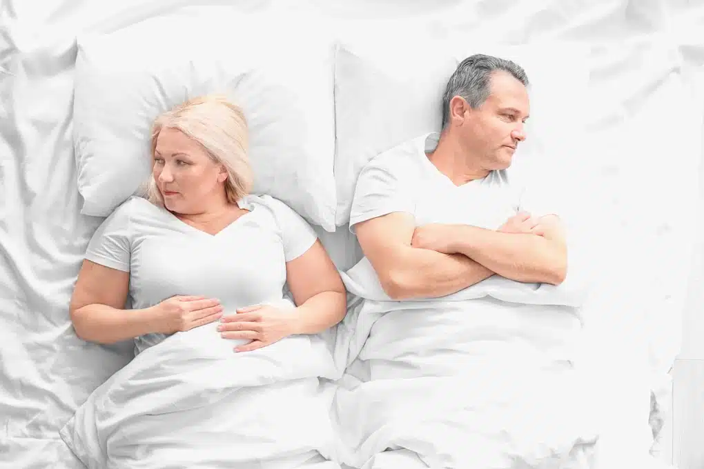 Middle Aged Couple lying on a white bed.