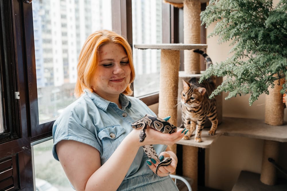Woman with acne scars holding a pet snake and having fun with her pet cat.